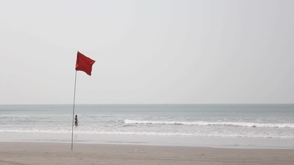 red flag in the wind on the background of a sandy beach and a girl in the sea