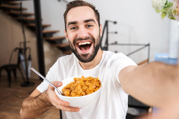 Happy man taking a selfie while sitting at the kitchen