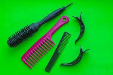 Barbershop. Tools stylist. Professional round hair styling brush, two combs and two large hair clips on bright green background.