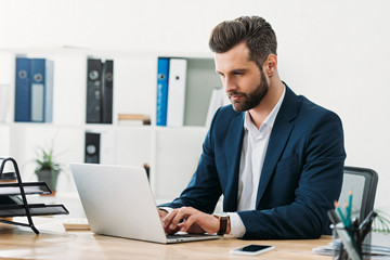 businessman in blue suit sitting at table with laptop and typing in office