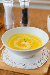 Classic Pureed Pumpkin Soup topping with Milk, Cream and Pepper. Served on wooden plate with salt, garlic and cutlery.