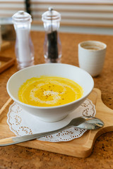 Classic Pureed Pumpkin Soup topping with Milk, Cream and Pepper. Served on wooden plate with salt, garlic and cutlery.