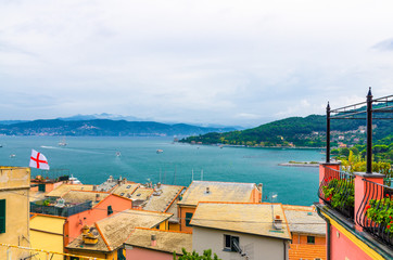 Top aerial view of Gulf of Spezia turquoise water, roofs of buildings in Portovenere, Palmaria island green hills, blue cloudy dramatic sky, Ligurian sea, Riviera di Levante, La Spezia, Liguria, Italy