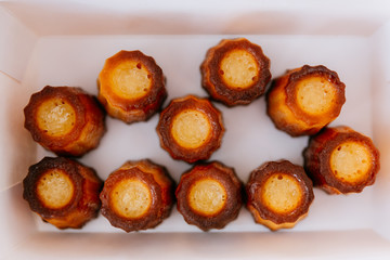 Top view of fresh baked Canelés inside white paper box. A small French pastry flavored with rum and vanilla with a soft and tender custard center and a dark, thick caramelized crust.