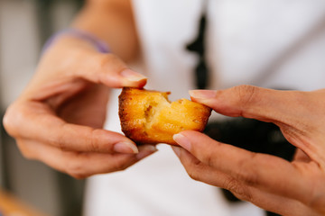 Female hands tearing fresh baked Canelés, A small French pastry flavored with rum and vanilla with a soft and tender custard center and a dark, thick caramelized crust.