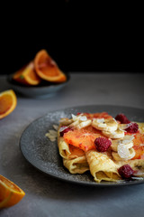 Crepes with bananas, blood orange slices and raspberries on a dark background