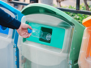 Closeup of man hand throwing empty plastic water bottle in recycling bin.