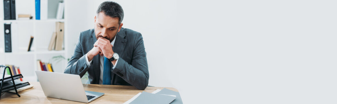 Handsome Businessman In Grey Suit Sitting At Table With Laptop And Thinking In Office