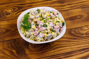 Tasty salad with sausage, green pea, canned corn, bell pepper, cucumber and mayonnaise on wooden table