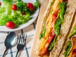 Close up of Sandwich with ham, cheese, tomatoes, lettuce, and toasted bread on the  wooden cutting board.
