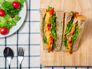 Close up of Sandwich with ham, cheese, tomatoes, lettuce, and toasted bread on the  wooden cutting board.