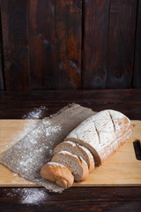 Fresh brown bread with sliced pieces on an oak board with scattered flour on a wooden background with a piece of linen fabric. Vertical photo