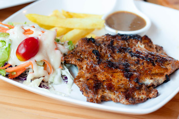 Chicken steak is a fast food, chicken steak this dish consists of with salad which has purple lettuce carrot tomato salad dressing french fries and black pepper sauce all in a white plate.