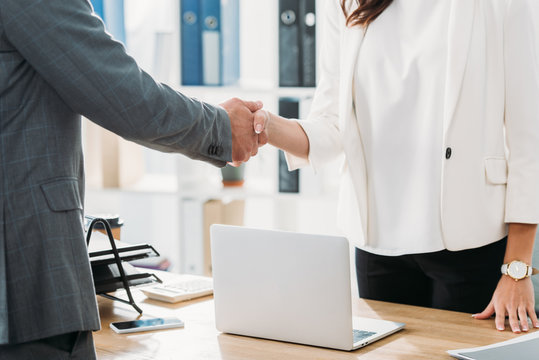 partial view of woman and man shaking hands at office