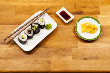 Homemade vegan Sushi rolls filled with avocado on a small plate on a wooden table with soy sauce, wasabi and ginger