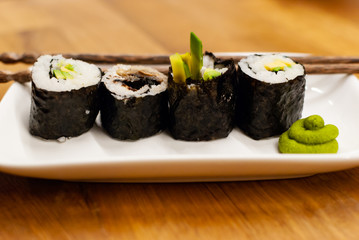 Homemade vegan Sushi rolls filled with avocado on a small plate on a wooden table with soy sauce, wasabi and ginger