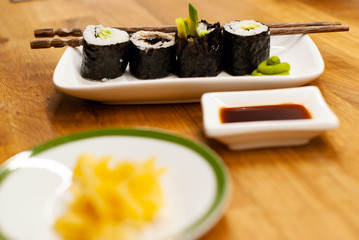 Homemade vegan Sushi rolls filled with avocado on a small plate on a wooden table with soy sauce, wasabi and ginger