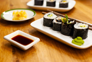 Homemade vegan Sushi rolls filled with avocado on a small plate on a wooden table with soy sauce, wasabi and ginger