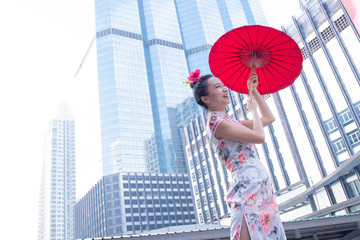 Pretty Asian woman wear Chinese national costumes (Qi Pao) and red umbrella, Travel in modern cities. Chinese new year concept