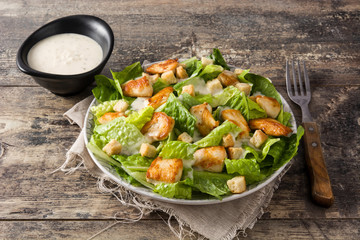 Caesar salad with lettuce,chicken and croutons on wooden table.
