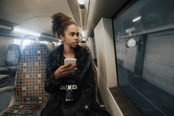 A young charming African-American female tourist with a modern film camera and smartphone is...