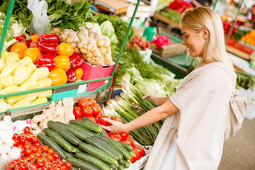 Cute young woman buying vegetables at the market
