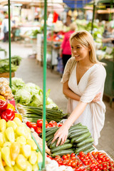Cute young woman buying vegetables at the market