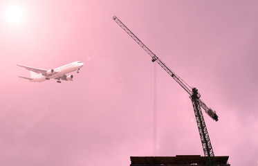 The bottom view through the construction cranes on the airliner in the cloudy sky. Sunset.