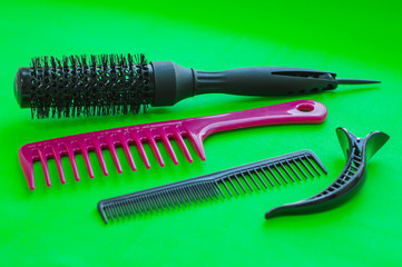 Barbershop. Tools stylist. Professional round hair styling brush, two combs and two large hair clips on bright green background.