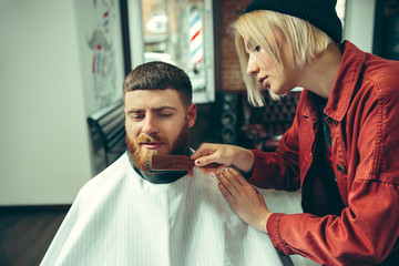Client during beard shaving in barbershop. Female barber at salon. Gender equality. Woman in the...