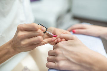 Obraz na płótnie Canvas Closeup of manicurist applying shiny red nail polish