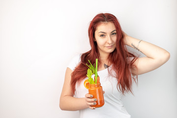 A young, healthy, smiling woman is holding a healthy, colorful smoothie in her hand