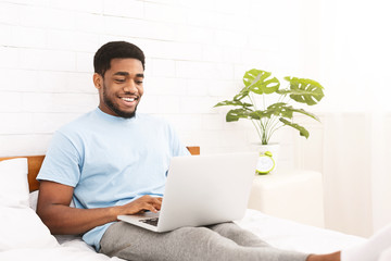 Young millennial guy using laptop in bed