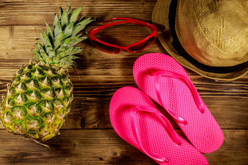 Summer holiday concept. Pineapple, straw hat, flip flops and sunglasses on wooden background