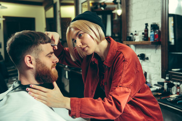 Client during beard shaving in barbershop. Female barber at salon. Gender equality. Woman in the...