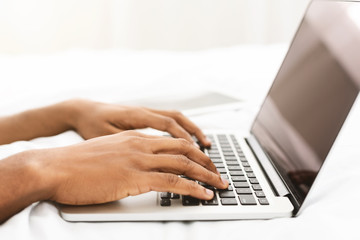 Black man blogger typing on laptop in bed