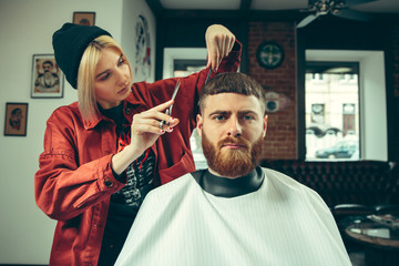 Client during beard shaving in barbershop. Female barber at salon. Gender equality. Woman in the male profession.