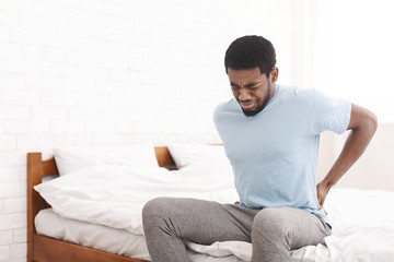 Man suffering from back pain at home in bedroom.