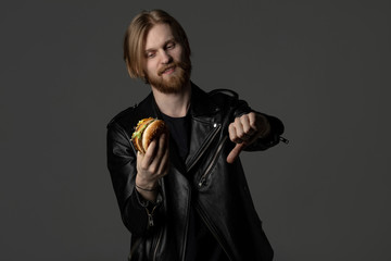 Bearded young man in leather jacket showing that burger is bad for your health