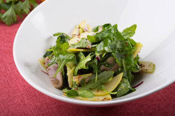 Green arugula salad with beef tongue and apple in a white bowl