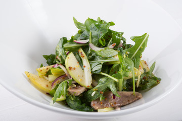 Green arugula salad with beef tongue and apple in a white bowl