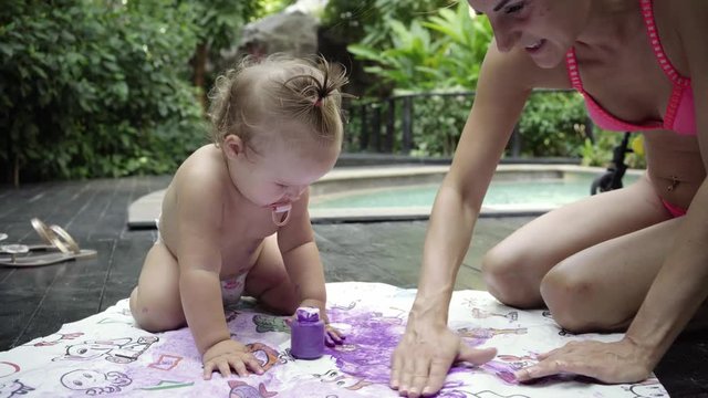 mother with the child paints finger paints by the pool in the garden. child development concept. 4k.
