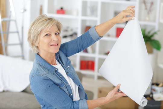 senior woman unrolling a wall paper on the wall