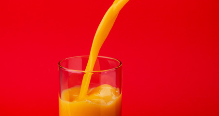 Orange juice pouring into glass, isolated on red color background, with copy space