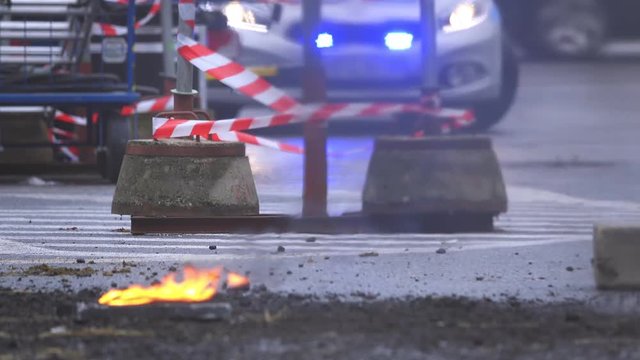 Police lights against red cordon tape on street burning debris and smoke