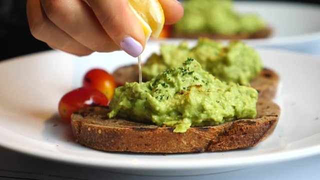 Closeup Of Hand Squeezes Lemon On Toast With Avocado. Breakfast Time, Healthy Food.