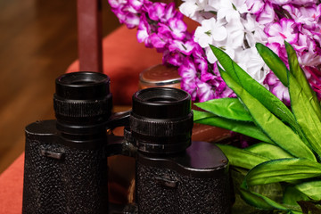 Black binoculars on the background of flowers