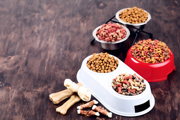 Dry pet food in bowls with bones on brown background