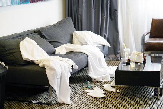 Mess In The Hotel Room. Scattered Bathrobes And Dirty And The Table With The Remnants Of Food And Plastic Cups.