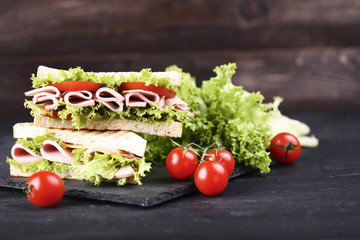 Sandwiches with ham, cheese and vegetables on black wooden table